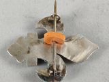 a silver flower brooch with an orange flower on it
