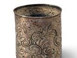 an old silver cup with a design on it on a white surface
