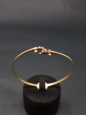 un bracelet rigide en or orné de pierres roses sur un fond noir