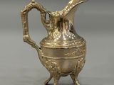 an antique silver plated pitcher on a stand on a gray background