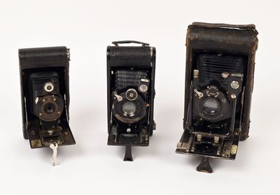 three old cameras sitting side by side on a white surface