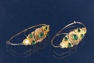 deux paires de boucles d'oreilles en or et émeraude posées sur un fond noir