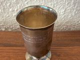 a silver cup on a wooden table with a white wall in the background