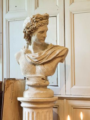 un buste d'homme assis sur un socle, à côté d'une bougie allumée