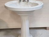 a white pedestal sink with two faucets on it