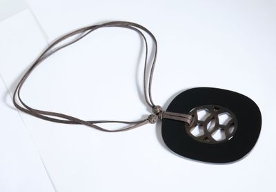 un collier composé d'un disque noir monté sur un cordon marron