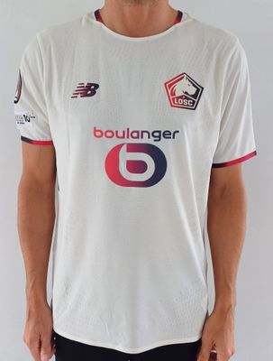 Cet homme porte une chemise blanche sur laquelle figure un numéro 6 rouge et bleu.