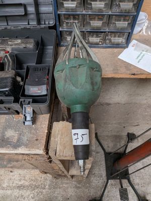 une perceuse verte posée sur une palette en bois, à côté d'une boîte à outils