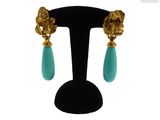 une paire de boucles d'oreilles turquoise et or posées sur un présentoir noir