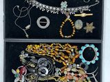 deux boîtes noires remplies de bijoux variés, posées sur une surface blanche