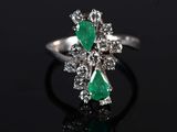 a close up of a diamond and emerald ring on a black surface