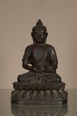 statue d'un Bouddha assis sur une fleur de lotus, dont le reflet se dégage sur une surface en verre