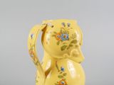 a yellow vase with a cat on it sitting on a table