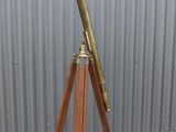 an antique brass telescope on a wooden tripod stands against a metal wall