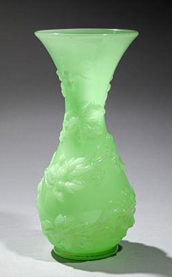 un vase vert posé sur une table, dont l'ombre se projette sur le sol