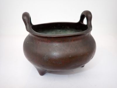 un petit pot marron muni d'anses, posé sur une surface blanche