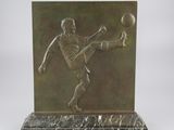 sculpture en bronze représentant un homme en train de frapper un ballon de football, posée sur un socle en marbre