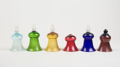 Quatre bouteilles en verre de couleurs différentes sont alignées sur une surface blanche.