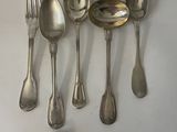 six spoons and a fork are arranged in a row on a white surface