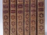 six old books lined up in a row on a white surface