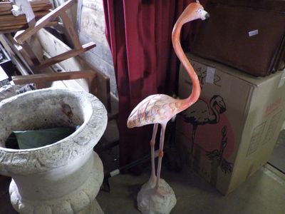 a pink flamingo standing next to a cement planter
