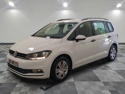 La Volkswagen Touran blanche est garée dans une pièce au sol carrelé en damier.