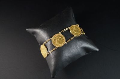 un gros plan sur un oreiller sur lequel est posé un bracelet composé de pièces d'or
