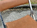 a brown leather folding chair sitting on the pavement