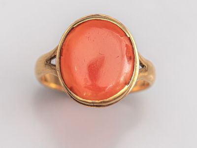 une bague en or ornée d'une pierre de corail ovale au centre