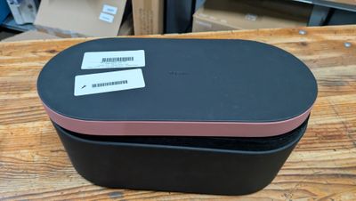 une boîte noire avec un couvercle rose posée sur une table en bois