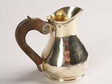 an antique silver pitcher with a wooden handle on a white surface