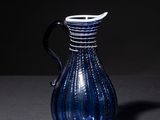 a blue glass pitcher with a black handle on a table