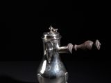 an antique silver teapot with a wooden handle on a black background