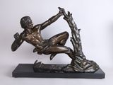 bronze statue of a man sitting on a tree branch with his hands in the air