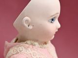 a close up of a baby doll sitting on a pink surface