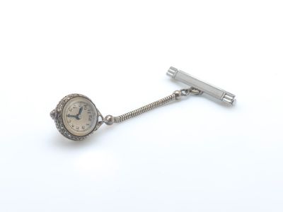 une montre en argent et une pince à cravate posées sur une surface blanche