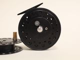 a black fly reel and a spool on a white surface