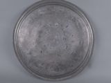 an old silver plate on a white surface with a gray background
