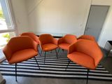 trois chaises orange et une table dans une pièce où se trouve un tapis rayé noir et blanc