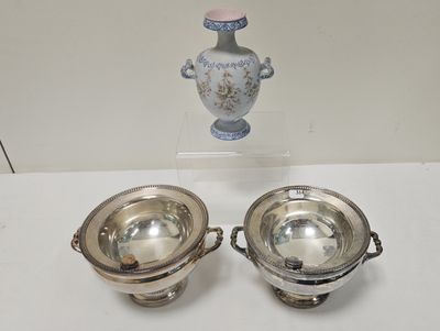 two silver dishes on a table with a vase in the background