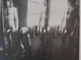 black and white photograph of two naked men standing in front of a mirror