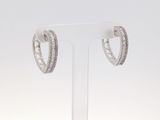 une paire de boucles d'oreilles créoles en or blanc et diamants, présentées sur un socle transparent