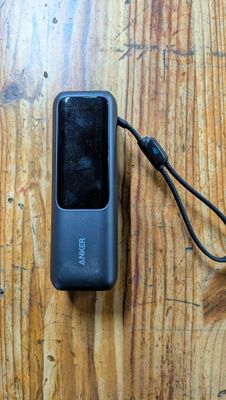 a cell phone that is connected to a charger on a wooden table