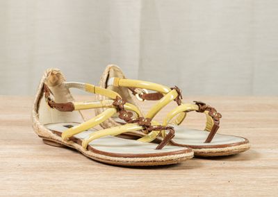 yellow and brown sandals on a wooden table with a curtain in the background