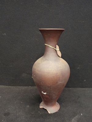 un vase marron posé sur une surface noire, près d'un mur noir