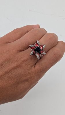 quelqu'un tient une bague sertie d'une pierre rouge et noire