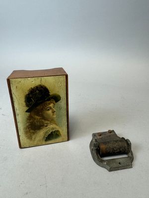 une petite boîte sur laquelle figure l'image d'une femme coiffée d'un chapeau, à côté d'une boucle de ceinture
