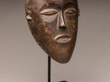 a close up of a wooden mask on a black stand