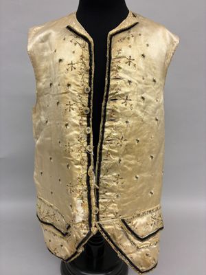 un gilet doré avec des bordures noires, posé sur une tête de mannequin