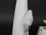 a white vase with a bird on it next to a white vase